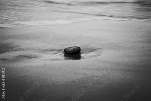 Grayscale shot of a stone on a sandy beach.