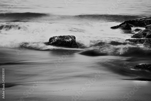 Grayscale shot of sea waves crashing the rocks at the beach.