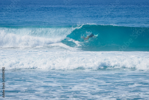 Male surfer dives under big wave with his surfboard. Shot from coast.