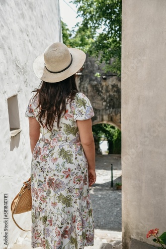 Vertical shot of a young female tourist in a floral dress and sunhat posing in an old town