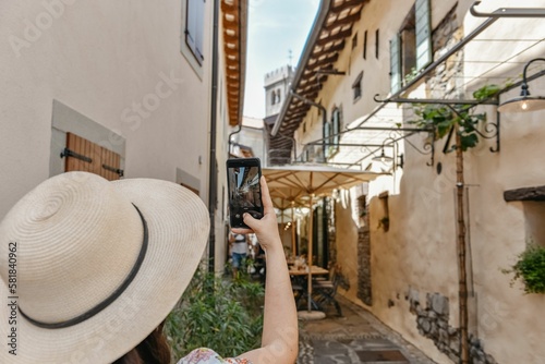 Young woman in a floral sundress and a straw hat taking pictures of the narrow streets of Smartno photo