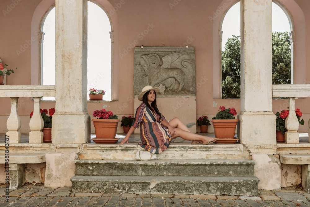 Stylish young woman sitting on stone stairs under arched columns of an old building