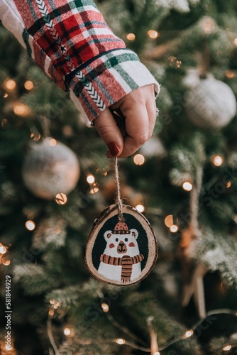 Female hand holding diy wooden handpainted christmas ornament in front of christmas tree