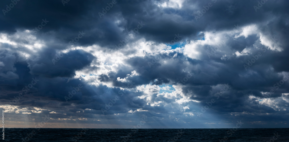 Panoramic view of the sunrays through the stormy clouds over the dark sea Panoramic view of the sunrays through the stormy clouds over the dark sea