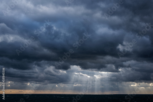 Distant sun rays through dark storm clouds over a dark sea
