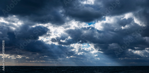 Panoramic view of the sunrays through the stormy clouds over the dark sea