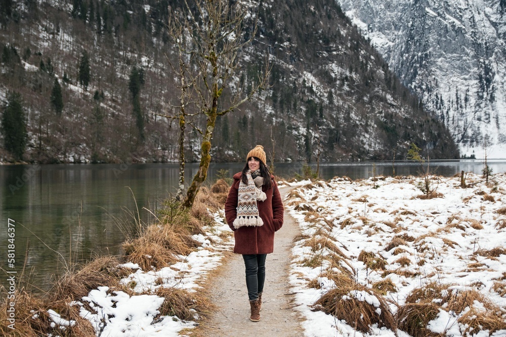 Adventurous girl in a brown coat and scarf walking on a trail at Lake Konigssee in Bavaria, Germany