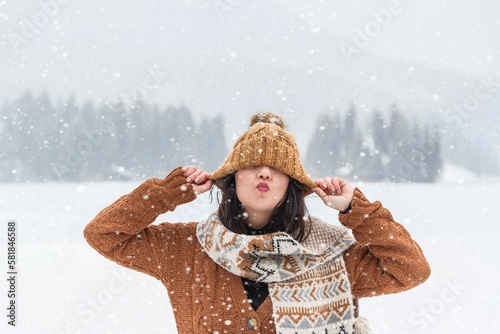 Woman in a cozy winter sweater and scarf pulling her hat over her eyes in a misty winter forest photo