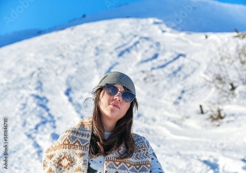 Female tourist with sunglasses and a scarf admiring the beautiful view on a snowy mountain