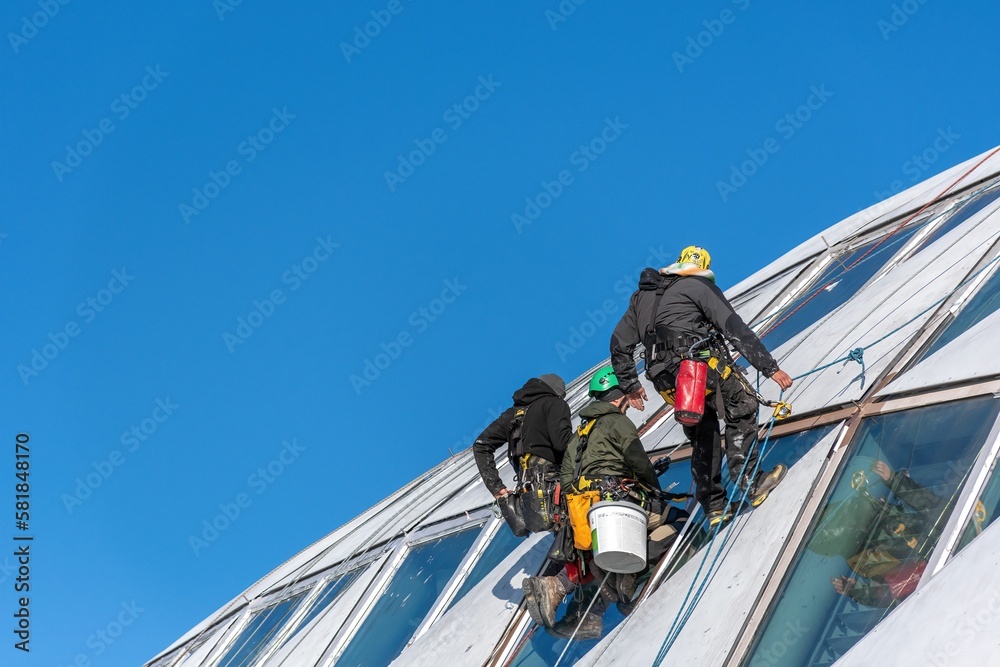 Professional window cleaners hanging on side of modern building against a blue sky