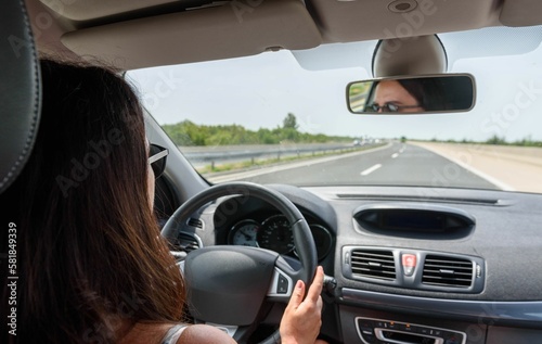 Rear view of young woman driving a car on motorway © Marko Klarić/Wirestock Creators