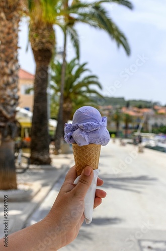 Vertical of a lavender ice cream cone held against thepalm trees in a vacation destination photo