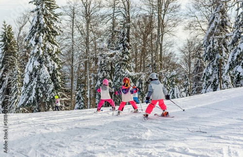 Scenic view of kids in ski school on a ski slope in a forest surrounded by snow