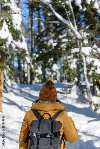 Vertical shot of a woman traveling in the snowy forest with a backpack - shot from back
