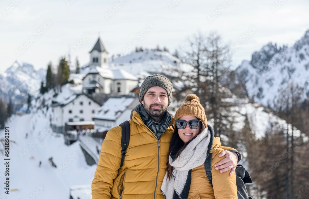 Fototapeta premium Couple in front of mountaintop village of Monte Lussari in Julian alps, Italy