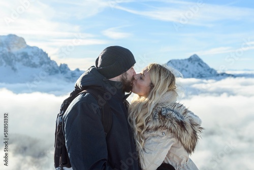 Side view of adorable couple kissing in the mountains with snow capped peaks on a sunny winter day