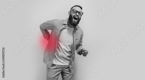 Portrait of a handsome caucasian guy isolated over white studio background showing how badly his back hurts, looking unhappy and exhausted