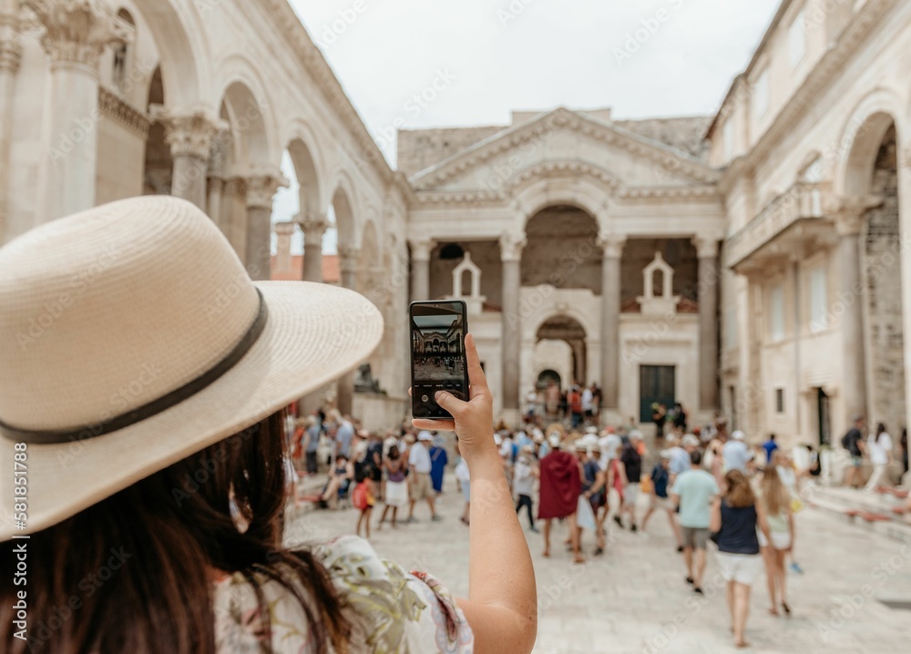 Rear view of woman taking a photo in a busy city square at Diocletian's palace in Split, Croatia