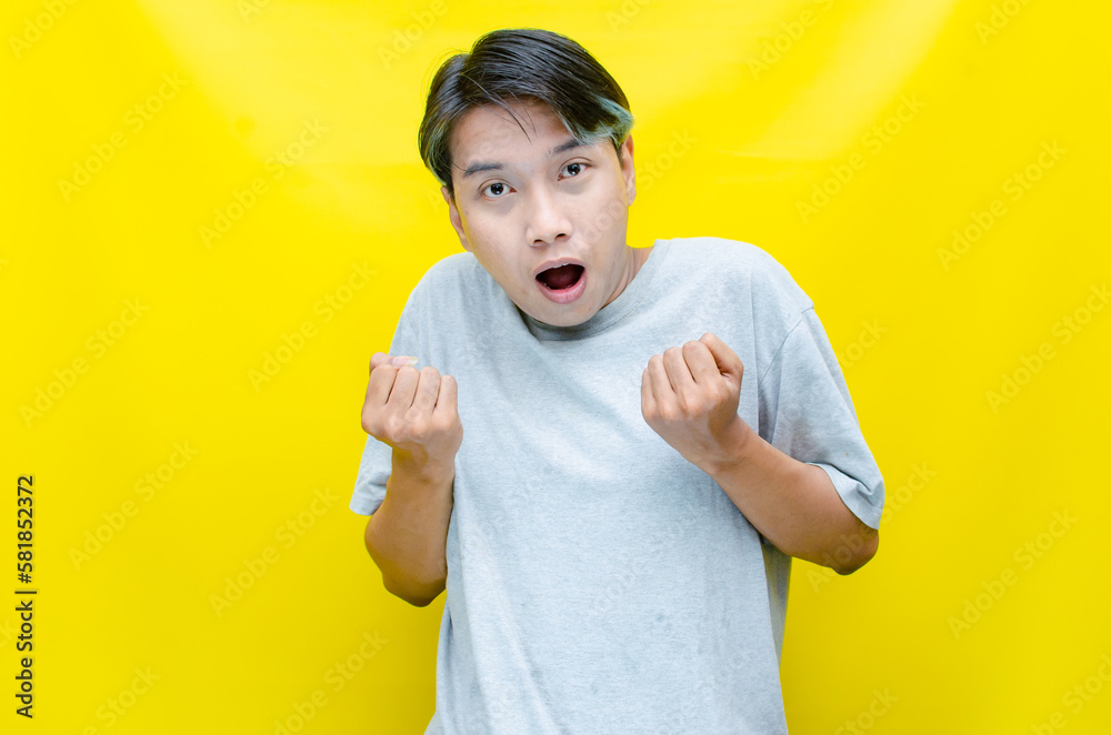 portrait of a happy young Asian man raising his hands in celebration of victory while laughing with joy. portrait of a happy young Asian man raising his hands in celebration of victory while laughing with joy.