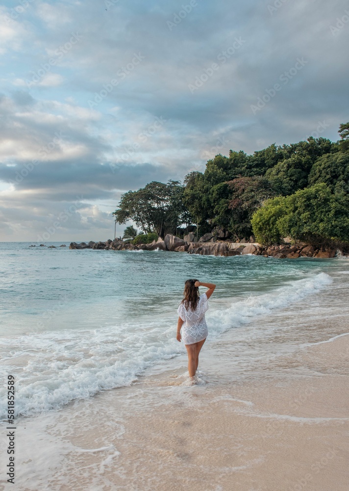 Young woman in beach cover-up walking on tropical sandy beach