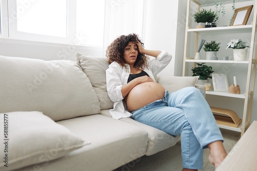 Pregnant woman headache lies at home in a shirt and jeans on the couch fatigue and heaviness in the last month of pregnancy before childbirth, lifestyle difficulties of motherhood, nausea