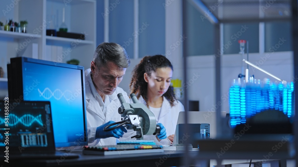 Team of lab scientists working on research, examining sample under microscope Team of lab scientists working on research, examining sample under microscope