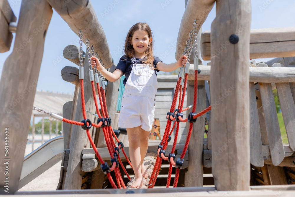 A happy little girl is playing on a wooden playground in summer on a sunny day. Children's Day