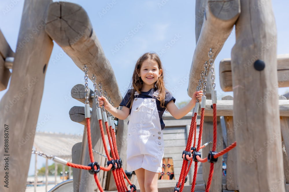 A happy little girl is playing on a wooden playground in summer on a sunny day. Children's Day