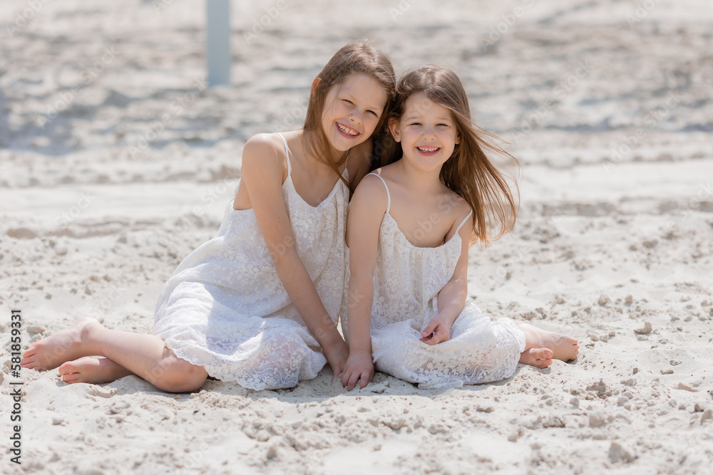 two happy little girls play on a white sandy beach near the ocean in summer. Children's holidays. Earth Day. Children's Day.Space for text