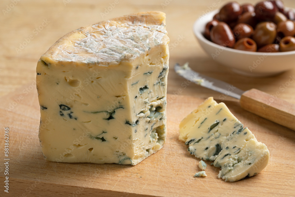 Piece of French blue Fourme d 'Ambert cheese and a piece on a cutting board for a snack Piece of French blue Fourme d 'Ambert cheese and a piece on a cutting board for a snack