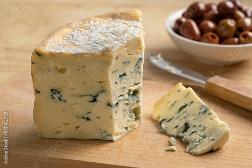 Piece of French blue Fourme d 'Ambert cheese and a piece on a cutting board for a snack