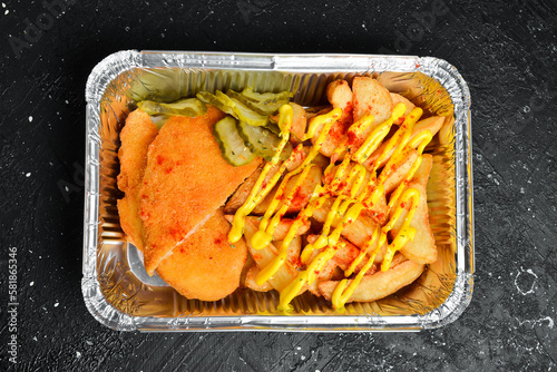Fast food. French fries and chicken schnitzel in a disposable dish. On a wooden board.