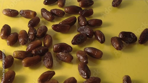 Dates. Dried date palm fruits. Healthy sweet snack food bowl. Pile of tasty dry dattes in plate. Date harvest symbolizing Ramadan. Slow motion. Pour on the table. Yellow background. photo