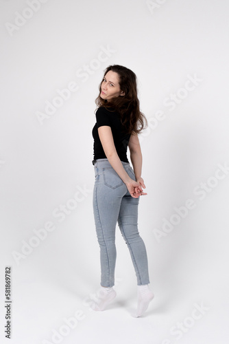 A young brunette girl of European appearance in a black T-shirt and blue jeans on a white background