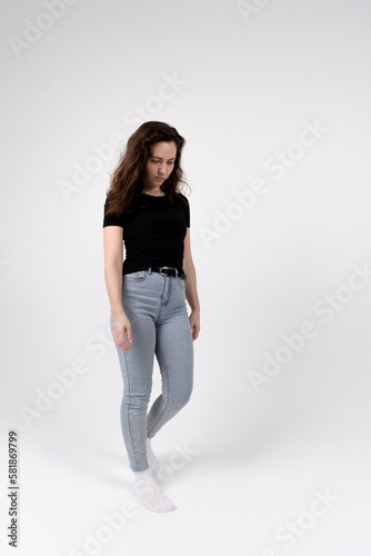 A young brunette girl of European appearance in a black T-shirt and blue jeans on a white background