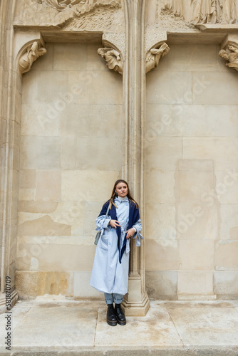 young woman with scarf on top of blue trench coat standing near historical building in Vienna.