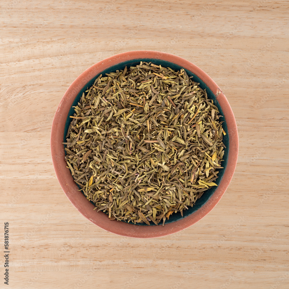 Top view of a small bowl with a portion of organic thyme leaf on a wood tabletop.