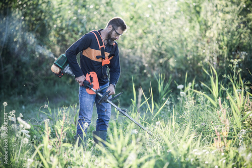 man trimming weed with weed trimmer in summer