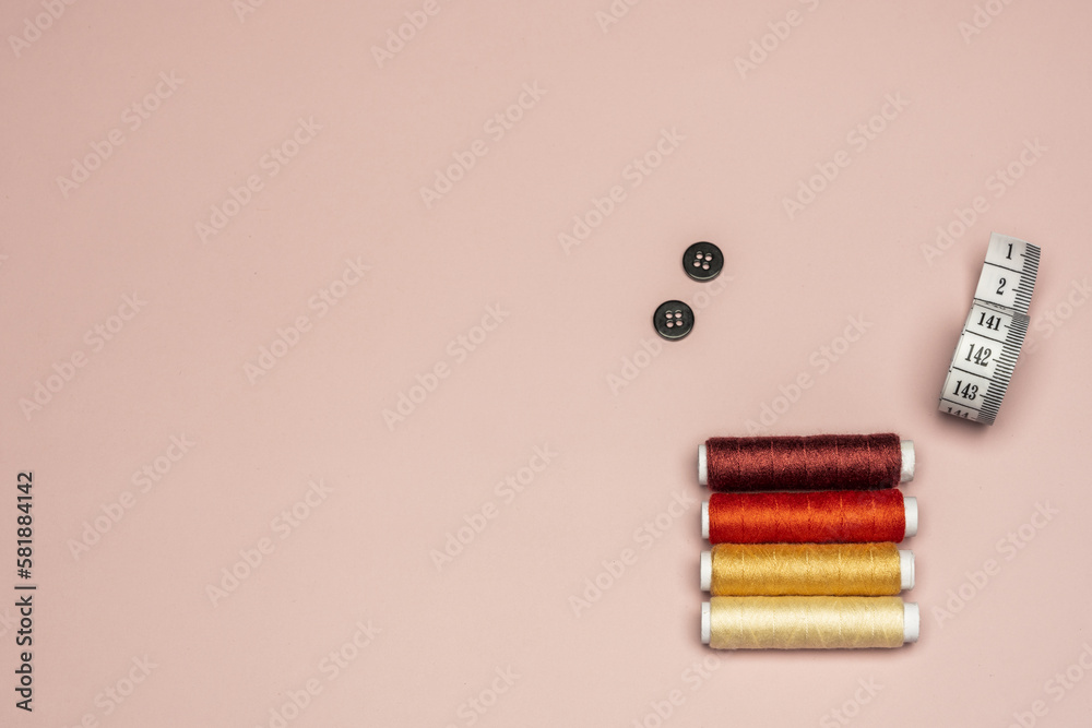 Still life with colored threads with black buttons and tape measure on a plain pink background Still life with colored threads with black buttons and tape measure on a plain pink background