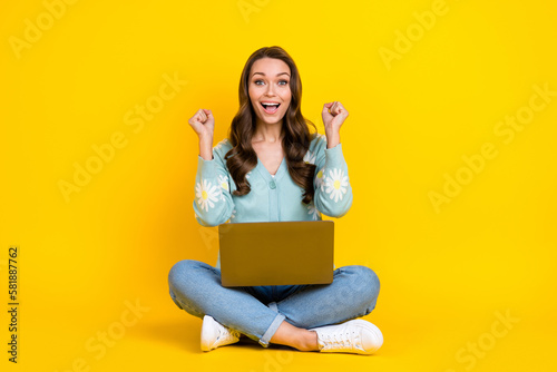 Full length photo of lucky cool woman wear turquoise cardigan rising fist winning game device isolated yellow color background © deagreez