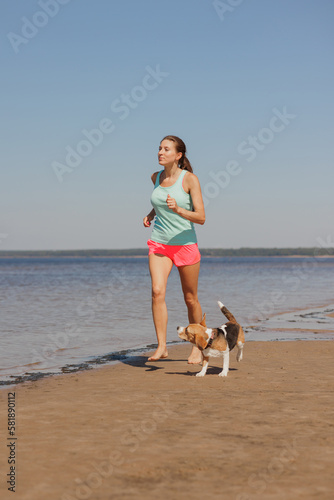 athletic woman and beagle dog run along sandy beach on seashore in morning. healthy lifestyle, train with your pet. fitness and yoga outdoor in nature. do sports for health © MyJuly