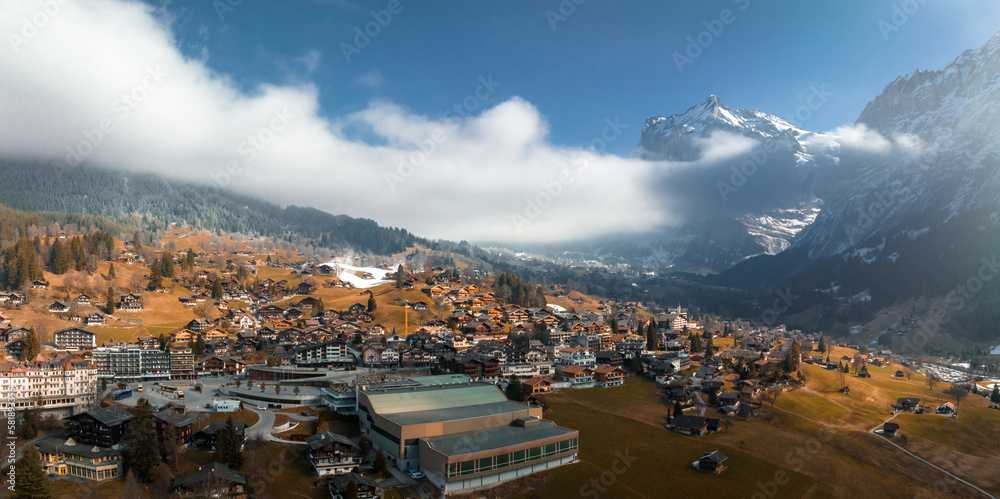 Aerial panorama of the Grindelwald, Switzerland village view near Swiss Alps mountains panorama landscape, wooden chalets on green fields and high peaks in background, Bernese Oberland, Europe.