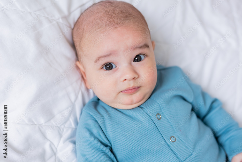 cute baby in a blue bodysuit is lying in bed. Top view cute baby in a blue bodysuit is lying in bed. Top view