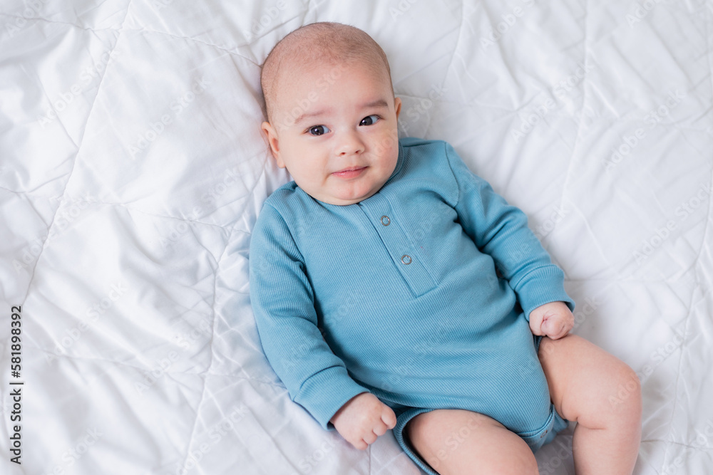 cute baby in a blue bodysuit is lying in bed. Top view cute baby in a blue bodysuit is lying in bed. Top view