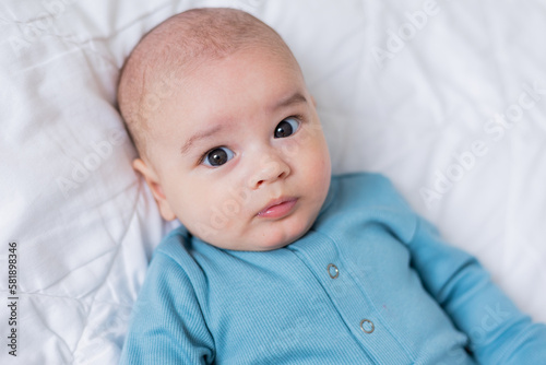portrait of a cute baby in a blue bodysuit lying on his back in a white bed. View from above. The child is 4 months old. Space for text