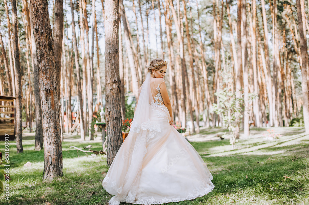 Beautiful, happy blonde model bride in a long white dress dances, spins in a pine face outdoors. Wedding photography, portrait.