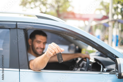 Close up at car key in young handsome man hand outta the windshield getting new car or rental a vehicle with happy and smiling. Male driving electricalc car on the road in his trip. photo