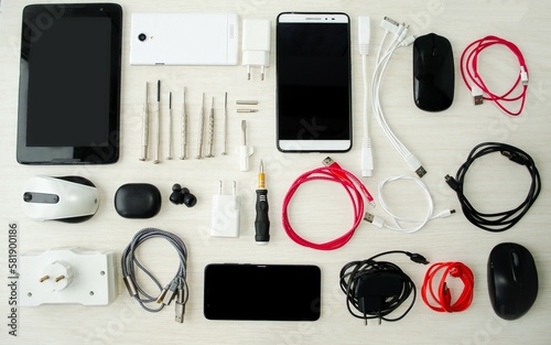 On a light background, electronic goods, phones, a tablet, a charger, screwdrivers, headphones, screwdrivers lie horizontally on the table in a row. The concept of electronic technology.