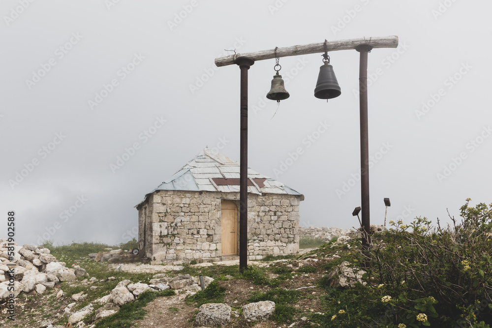 Old stone orthodox Saint Giorgi Church in Khvamli Mountain range in Georgia with simple wooden belfry with two bells, foggy weather.