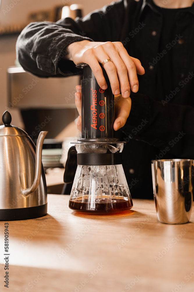 Barista is pushing aeropress for pouring coffee drops trought aeropress to pot. Alternative scandinavian coffee brewing method. Aeropress coffee.
